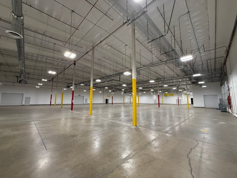 Empty warehouse interior with polished concrete floor, yellow and red support columns, and LED ceiling lights