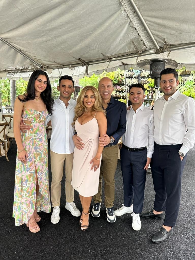 Six people standing together under a tent at an outdoor event, wearing casual and smart casual clothing